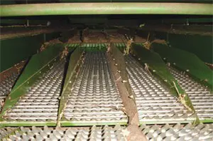 A imagem oferece uma visão interna e detalhada do sistema de peneiras de uma colheitadeira agrícola. O foco está nas grelhas