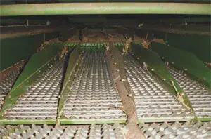 Mecanismo Interno da Colheitadeira: Peneiras e Separação A imagem oferece uma visão interna e detalhada do sistema de peneiras de uma colheitadeira agrícola. O foco está nas grelhas