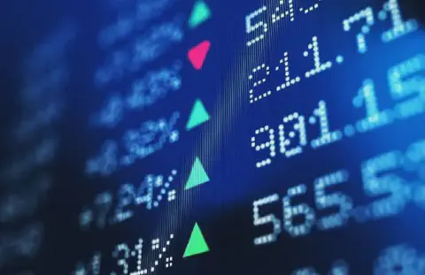 close-up de uma tela digital com dados do mercado financeiro, apresentada em um ângulo dinâmico. O fundo é