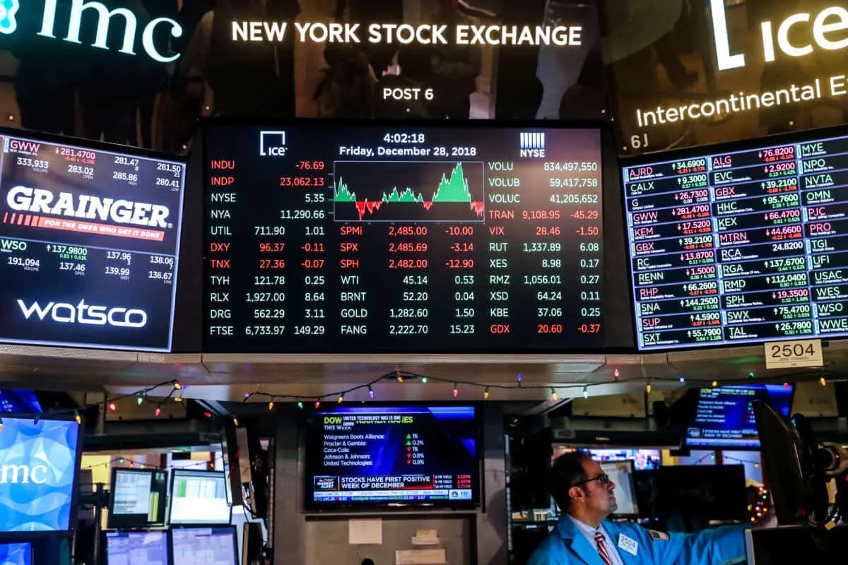 ambiente dinâmico do pregão da Bolsa de Valores de Nova York (NYSE). Em primeiro plano, diversos painéis e