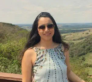 o retrato de uma mulher jovem, de cabelos escuros e longos, usando óculos de sol e sorrindo para a câmera. Ela