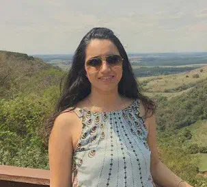 o retrato de uma mulher jovem, de cabelos escuros e longos, usando óculos de sol e sorrindo para a câmera. Ela