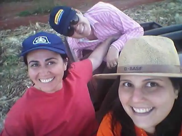 Mulheres no Agronegócio: A Força Feminina no Campo selfie casual de três mulheres sorrindo em um ambiente rural, provavelmente uma fazenda ou campo agrícola. O f