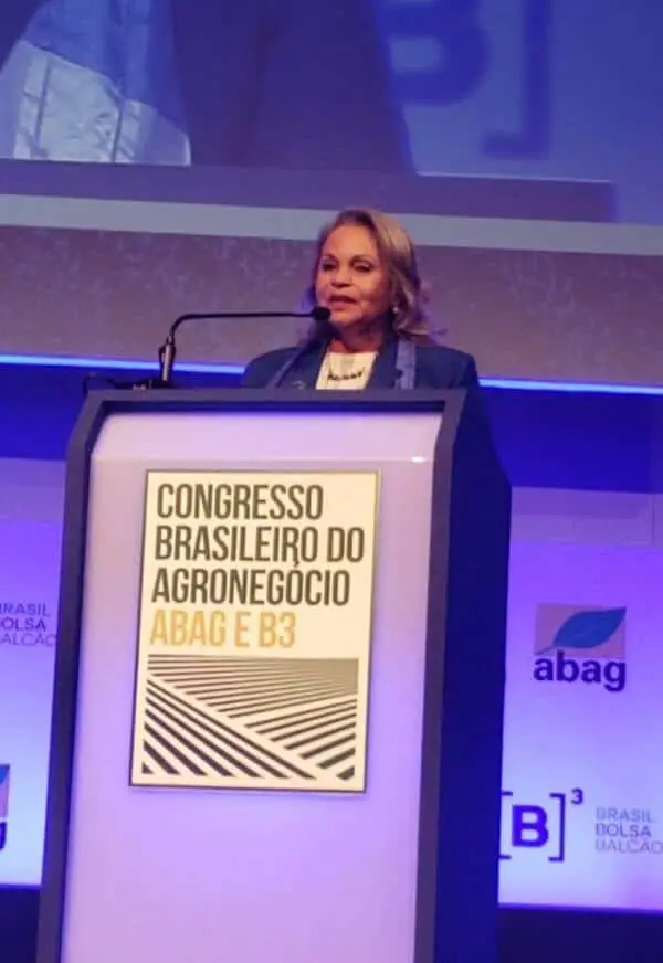 Palestra no Congresso Brasileiro do Agronegócio ABAG e B3 mulher discursando em um púlpito durante um evento formal. Ela está vestida profissionalmente com um bla