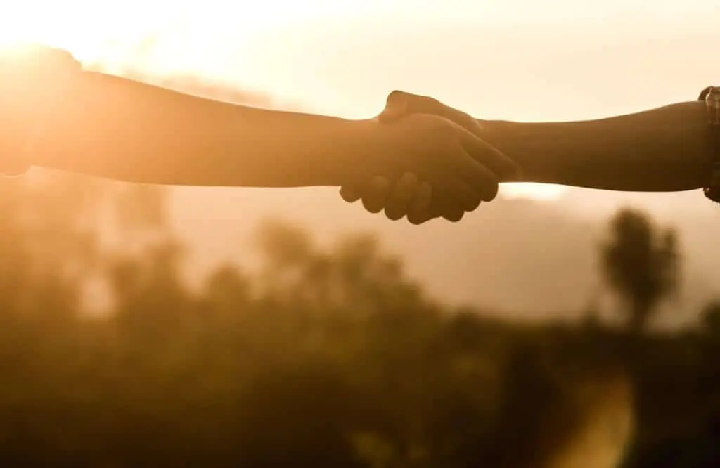 imagem captura em close-up o momento de um aperto de mão entre duas pessoas, silhuetado contra a luz quente e dourada de um