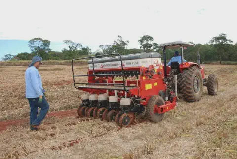 operação de plantio mecanizado em uma área rural. Em primeiro plano, um trator vermelho de grande porte