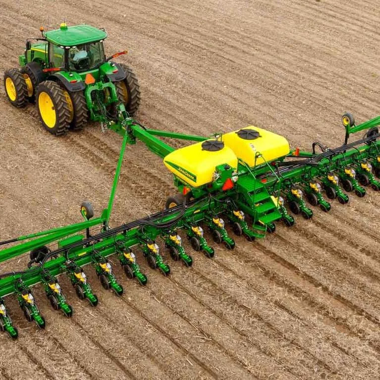 uma visão aérea de um trator John Deere, de cor verde e amarela, operando em um campo agrícola. O trator, equi