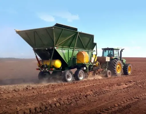 uma operação agrícola em larga escala, destacando um trator verde de grande porte tracionando um implemento ro