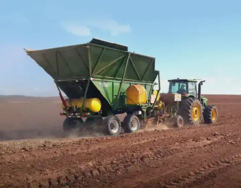 uma operação agrícola em larga escala, destacando um trator verde de grande porte tracionando um implemento ro