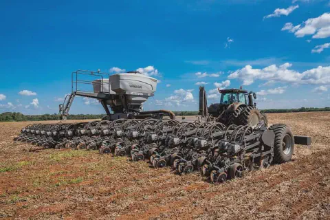 uma operação de plantio em larga escala em um dia ensolarado. Em primeiro plano, um trator moderno e robusto e