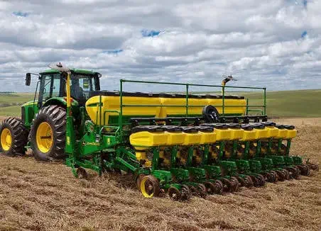 trator agrícola verde e amarelo da marca John Deere, acoplado a uma grande semeadora (ou plantadeira) da me