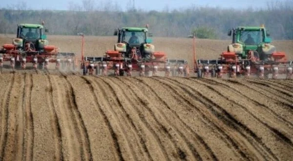 uma operação agrícola de grande escala, destacando três tratores verdes, equipados com semeadoras/plantadeiras