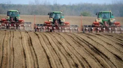 uma operação agrícola de grande escala, destacando três tratores verdes, equipados com semeadoras/plantadeiras