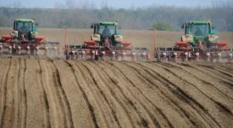 uma operação agrícola de grande escala, destacando três tratores verdes, equipados com semeadoras/plantadeiras