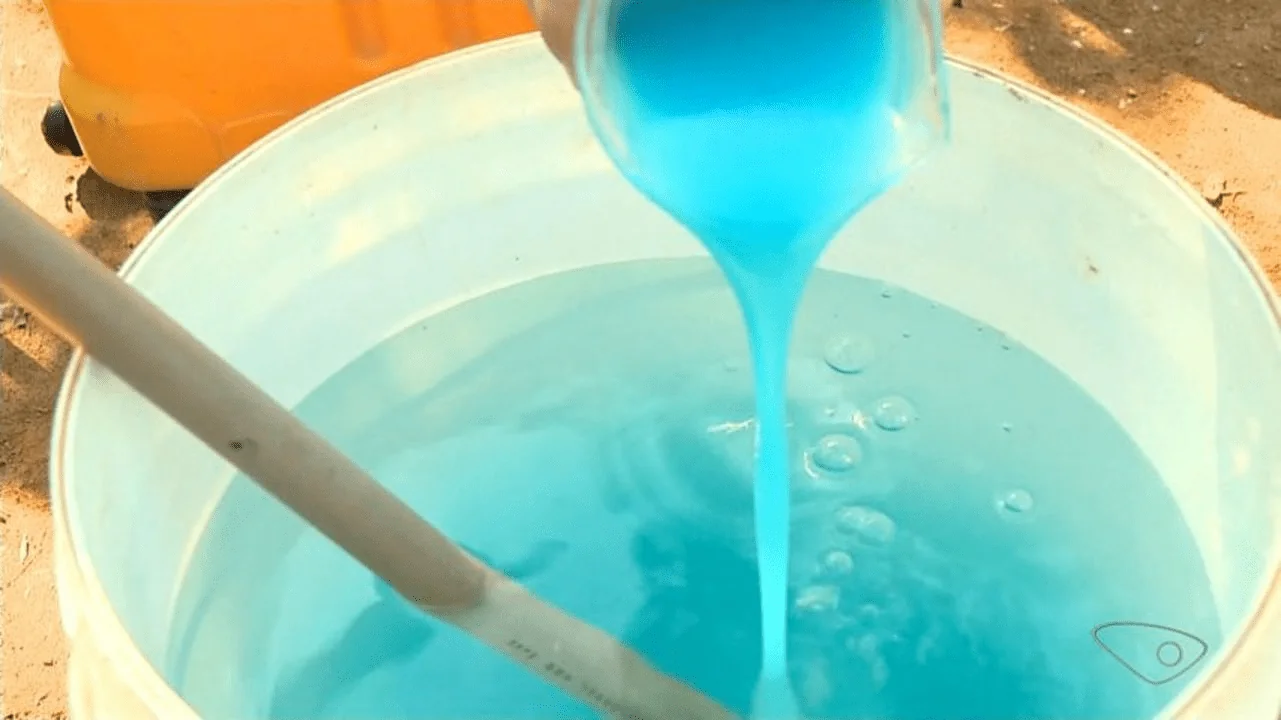 close-up do processo de preparação de uma calda agrícola. Um líquido azul, viscoso e concentrado está send