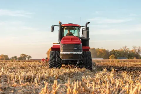 trator agrícola de grande porte, na cor vermelha, visto de frente em um campo recém-colhido, provavelmente