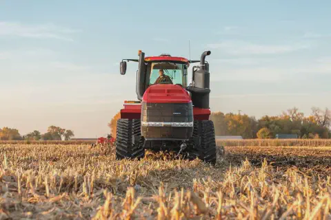 trator agrícola de grande porte, na cor vermelha, visto de frente em um campo recém-colhido, provavelmente