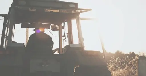 silhueta de um agricultor dentro da cabine de um trator, visto por trás, contra a luz intensa do sol nasce