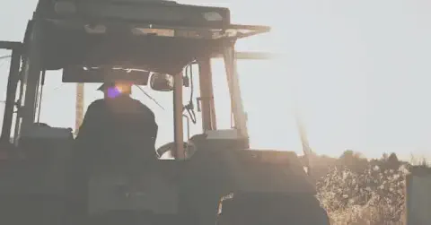 silhueta de um agricultor dentro da cabine de um trator, visto por trás, contra a luz intensa do sol nasce