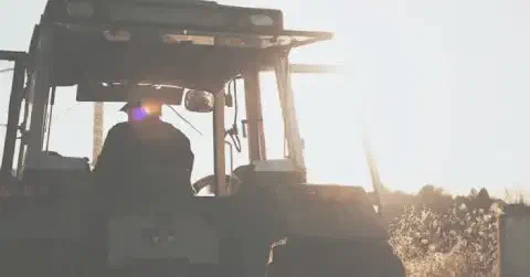 silhueta de um agricultor dentro da cabine de um trator, visto por trás, contra a luz intensa do sol nasce