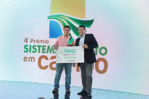 momento de premiação durante o '4º Prêmio Sistema FAMATO em Campo'. Dois homens estão em destaque no palc