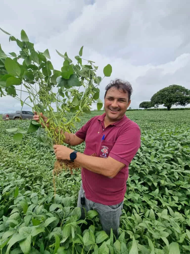 agricultor ou engenheiro agrônomo sorridente, em pé no meio de uma extensa lavoura de soja. Ele veste uma