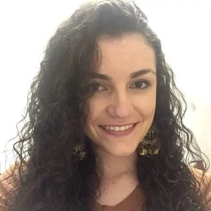 retrato em close-up de uma mulher jovem, sorrindo de forma calorosa e direta para a câmera. Ela possui cabelos