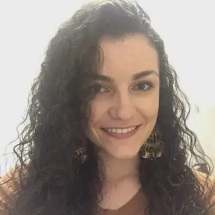 retrato em close-up de uma mulher jovem, sorrindo de forma calorosa e direta para a câmera. Ela possui cabelos