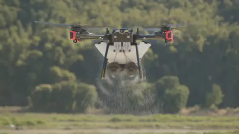 drone agrícola profissional em pleno voo, pairando a baixa altitude sobre uma lavoura. O equipamento, um