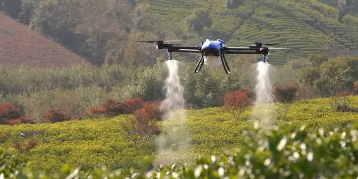 drone agrícola profissional, de cor azul e preta, em pleno voo sobre uma extensa plantação. O equipamento e