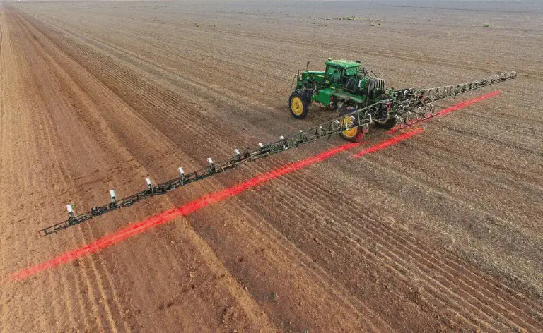 Pulverização Localizada: Tecnologia e Precisão no Campo uma visão aérea de um pulverizador agrícola de grande porte, acoplado a um trator verde, operando em uma vasta