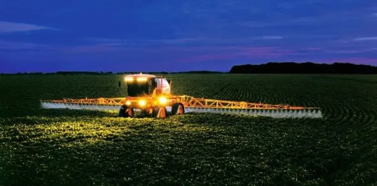Pulverizador agrícola em aplicação noturna na lavoura operação agrícola noturna em uma vasta lavoura, provavelmente de soja ou milho em estágio inicial. No ce
