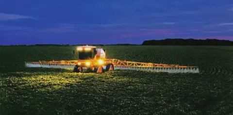 operação agrícola noturna em uma vasta lavoura, provavelmente de soja ou milho em estágio inicial. No ce