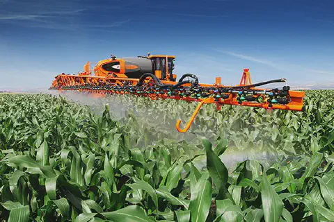 pulverizador autopropelido de grande porte, de cor laranja e preta, em plena operação numa vasta lavoura de