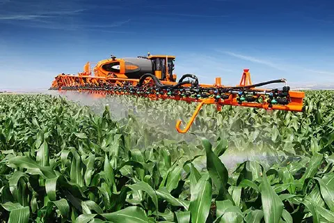 pulverizador autopropelido de grande porte, de cor laranja e preta, em plena operação numa vasta lavoura de