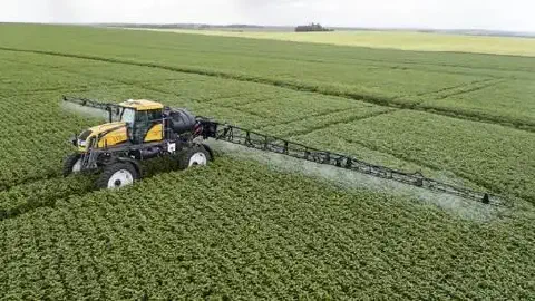 uma visão aérea de um pulverizador autopropelido, de cor amarela e preta, em plena operação numa vasta lavoura