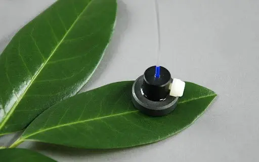 pequeno e sofisticado sensor eletrônico posicionado sobre uma folha verde e saudável, contra um fundo neutr