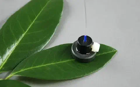 pequeno e sofisticado sensor eletrônico posicionado sobre uma folha verde e saudável, contra um fundo neutr