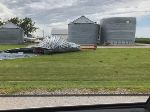 o cenário de uma propriedade rural após um evento climático severo. Em primeiro plano, um grande silo de grã