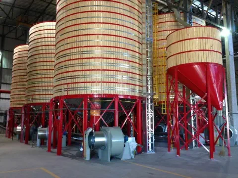 uma fileira de grandes silos de armazenamento localizados dentro de um galpão industrial. Essas estruturas cil