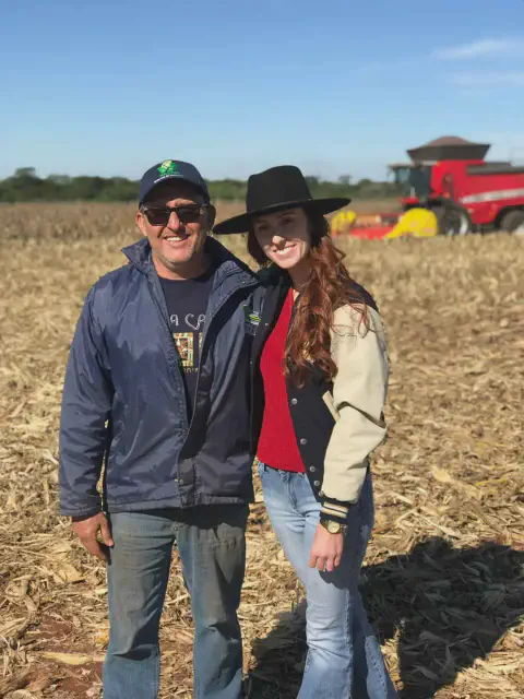 homem e uma mulher, possivelmente pai e filha ou colegas de trabalho, posando sorridentes em um campo de