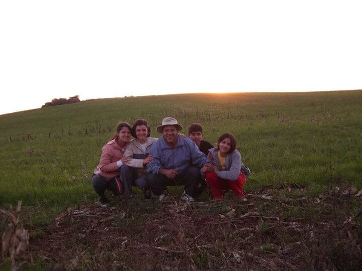 família de cinco pessoas – um casal e três filhos – agachados juntos em um campo verdejante, posando par