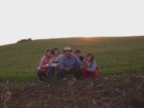 família de cinco pessoas – um casal e três filhos – agachados juntos em um campo verdejante, posando par