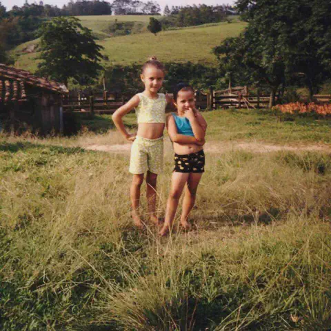 cena nostálgica e afetuosa da vida no campo, mostrando duas meninas, provavelmente irmãs ou amigas, posa