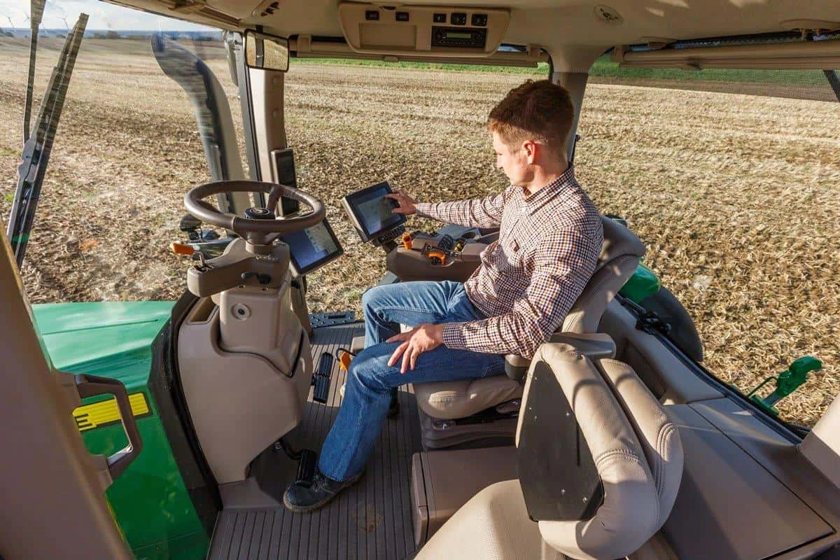 interior da cabine de um trator moderno, onde um jovem agricultor está sentado no assento do operador. Ele