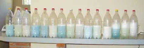 uma fileira de garrafas PET transparentes alinhadas sobre uma bancada, cada uma contendo uma quantidade de líq