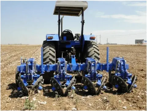 a traseira de um trator azul de médio porte, parado em uma lavoura sob um céu claro e ensolarado. Acoplado ao