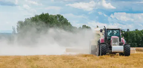 cena dinâmica de uma operação agrícola em um dia ensolarado. Em primeiro plano, um trator vermelho de gr