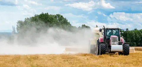 cena dinâmica de uma operação agrícola em um dia ensolarado. Em primeiro plano, um trator vermelho de gr