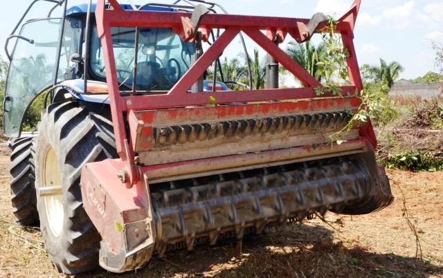 close-up da parte traseira de um trator agrícola de cor azul, ao qual está acoplado um robusto implemento v
